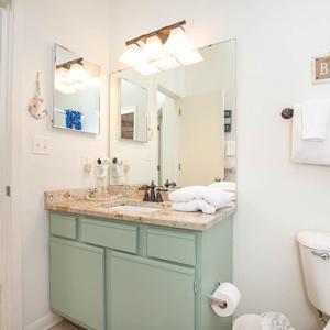 Bathroom features a light green vanity with a stylish countertop, plush towels, and a cozy chair visible in the background