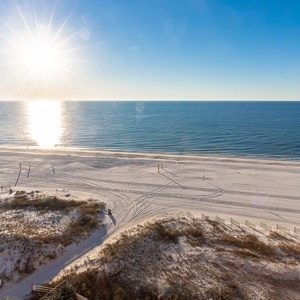 The sun glistens over the calm water, illuminating the pristine white sand beach and inviting a serene beach experience