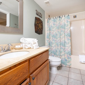 The bathroom features a light-colored vanity with a large mirror, a floral shower curtain, and neatly arranged towels