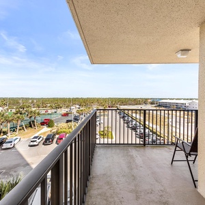 A spacious balcony offers a view of the surrounding greenery and parking area, with a comfortable chair for relaxation