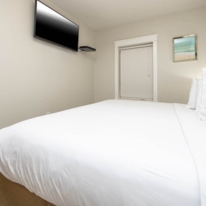 A cozy guest bedroom features a plush king bed with crisp linens, a mounted TV, and cheerful beach artwork on the walls