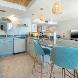 The open kitchen design features smart appliances, a stylish countertops, and a  dining area with turquoise bar stools