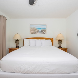 The bedroom features a comfortable bed, stylish lamps, and a beach-themed artwork, perfect for a relaxing getaway