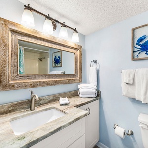 The guest bathroom features a stylish mirror, marbled countertop, and beach-themed artwork, creating a refreshing atmosphere