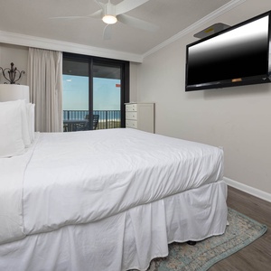 Bright and airy master bedroom features a king bed, a mounted TV, and a sliding door leading to a balcony with a gulf view
