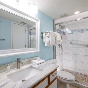 The bathroom features a sleek marbled countertop, a spacious walk-in shower, and soft towels neatly arranged on a rack