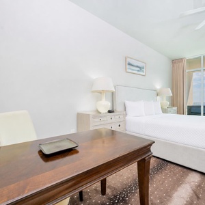 The master bedroom features a plush bed, a stylish desk, and a stunning beachfront view from the large windows