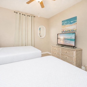 Relax in this cozy guest bedroom featuring two double beds, a TV, and beach decor for a comfortable stay