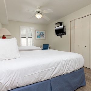 Rest in this inviting guest bedroom featuring two double beds, a TV, and natural light streaming through the shutters