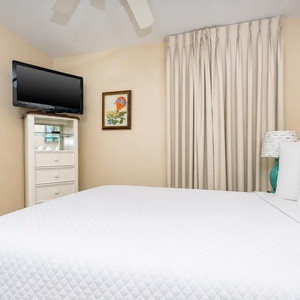 Guest bedroom featuring a plush queen bed, wall-mounted TV, and soft beige tones for a relaxing retreat