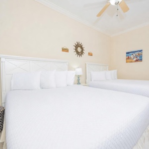 Relaxing guest bedroom featuring two cozy queen beds, soft white linens, and cheerful beach-themed decor