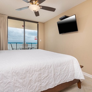 The master features a plush king bed, a wall-mounted TV, and a sliding door leading to a balcony with a beach view