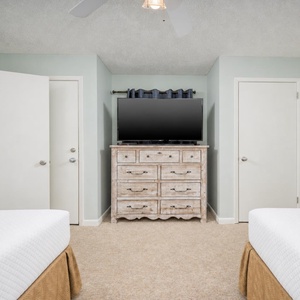 Guest bedroom features two double beds, a wooden dresser with a TV, and light green walls creating a calming atmosphere