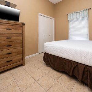 Cozy guest bedroom featuring a two comfortable queen beds, wooden dresser with a TV, and a window for natural light