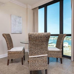 Dine at the glass table surrounded by woven chairs, with a serene view of the water through large windows