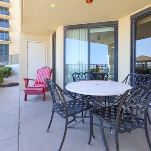 Outdoor patio featuring a round table with black metal chairs and a red lounge chair, perfect for relaxing by the beach