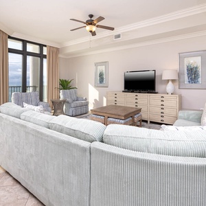 This living area features a plush sectional sofa, a flat-screen TV, and stunning beachfront views through large windows
