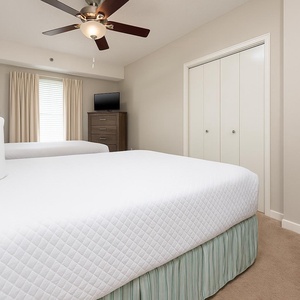 Cozy guest bedroom featuring two double beds, a dresser, and a TV, with natural light streaming through the window