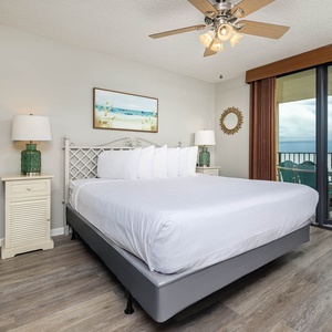 Master bedroom featuring a king bed, coastal artwork, and sliding glass doors leading to a balcony with beach front views