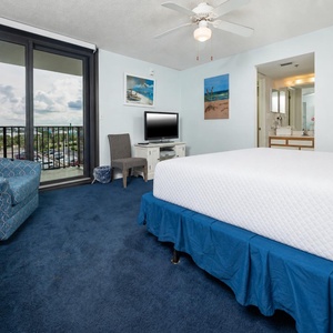 Blue carpet complements the cozy king in the master, while a sliding door leads to a balcony with a view of the surroundings