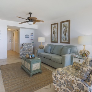 The living area features a light blue sofa, patterned armchair, and coastal decor, creating a relaxed beach vibe