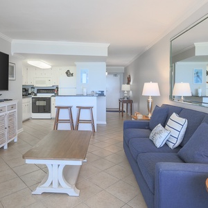 The living area features a comfortable sofa, a large TV, and a view into the well-equipped kitchen, perfect for relaxation