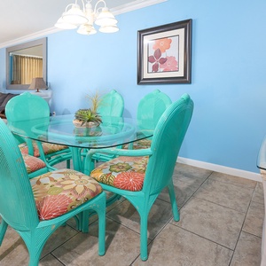 Turquoise dining chairs surround a glass table, complemented by colorful cushions and a decorative plant centerpiece