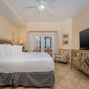 The master bedroom features a large king bed, a TV, and French doors leading to a lovely outdoor area