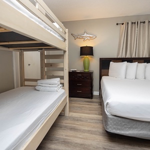 The guest bedroom features a twin bunk bed, a queen bed with plush pillows, and a decorative fish wall accent