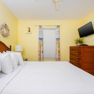 This cozy bedroom features a plush bed, bright yellow walls, and a wall-mounted TV for relaxing evenings