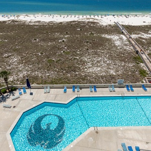 Pool area with lounge chairs and a pathway leading to the beach, framed by lush greenery and vibrant umbrellas