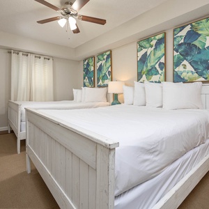 Guest bedroom featuring two cozy queen beds, a stylish dresser, and tropical artwork, creating a relaxed atmosphere