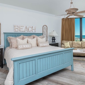 Relax in the master suite bedroom featuring a king bed, coastal decor, sofa with queen sleeper, and balcony beach views