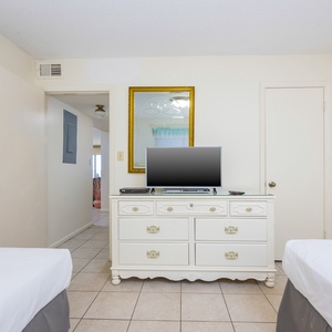 This guest bedroom features two beds, a TV on a stylish white dresser, and a welcoming view into the hallway