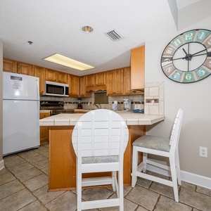 Bright wood cabinetry complements the kitchen, featuring a breakfast bar with white stools and a stylish wall clock