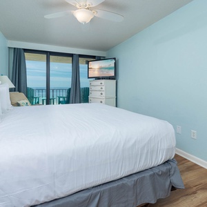 The master bedroom features a large king bed, a TV for entertainment, and a stunning view from the balcony