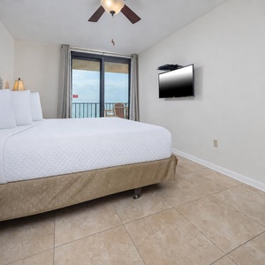 The master bedroom features a comfortable king bed, a wall-mounted TV, and a beautiful view from the balcony