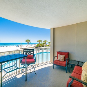 Relax on the private balcony with cozy seating, overlooking the sparkling pool and pristine beach beyond