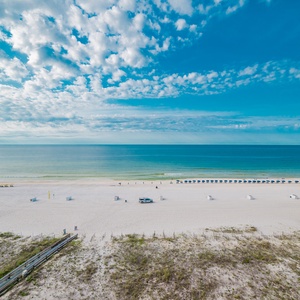 Serene view of the beach front features white sand and colorful umbrellas under a bright blue sky with scattered clouds