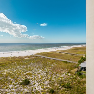 Gulf views stretch across the white sand beach, framed by lush greenery and a private balcony with seating
