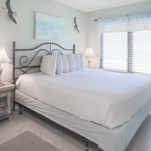 The master bedroom features a comfortable bed, stylish decor, and large windows that offer a beachfront view