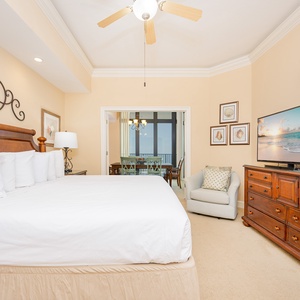 Bright and inviting bedroom featuring a cozy king bed, large TV, and a lovely view of the dining area