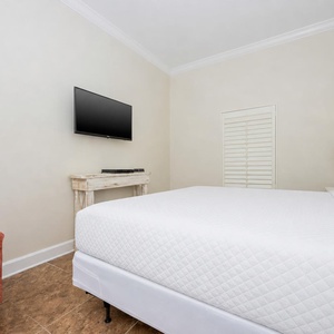 Inviting guest bedroom featuring a king bed, a cozy chair, and a wall-mounted TV for entertainment