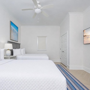 Relax in this guest room featuring two comfortable queen beds, coastal artwork, and a large TV