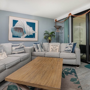 The living area features a gray sectional, queen sleeper sofa, nautical decor, and a balcony with a beautiful beach view