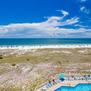 Vibrant beach umbrellas dot the shoreline, overlooking the inviting pool area and the expansive Gulf waters beyond