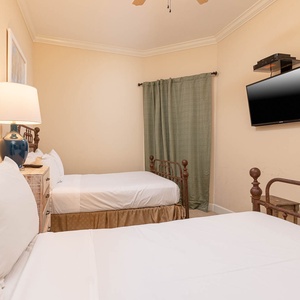 This cozy guest bedroom features two vintage iron beds, a TV for entertainment, and soft beige walls for a warm ambiance