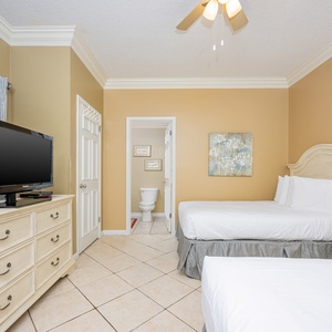 Cozy guest room featuring two double beds, a TV on a dresser, and a view into the bathroom area with tasteful art on the wall