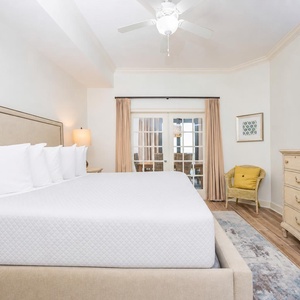The master bedroom features a plush king bed, a large TV, and access to a cozy balcony area through French doors