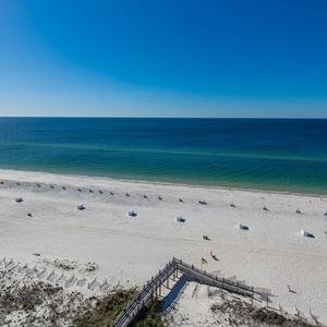 A serene view of the beach front features white sand and gentle waves under a clear blue sky, inviting relaxation